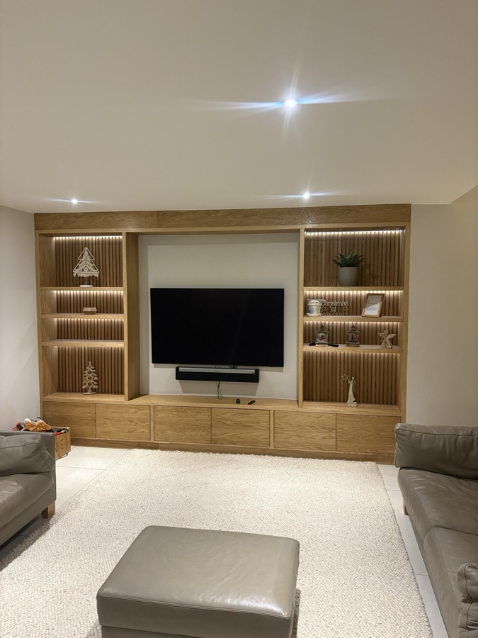 Slatted oak media wall with warm LED display niches and twin leather sofas